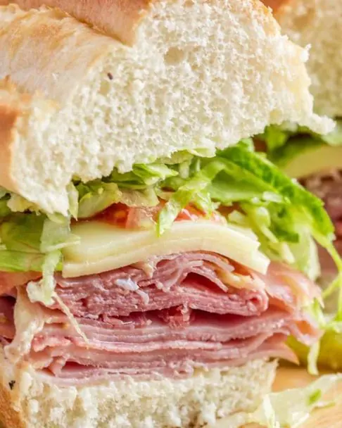 Sub roll stacked with sliced ham, cheese, lettuce and tomato