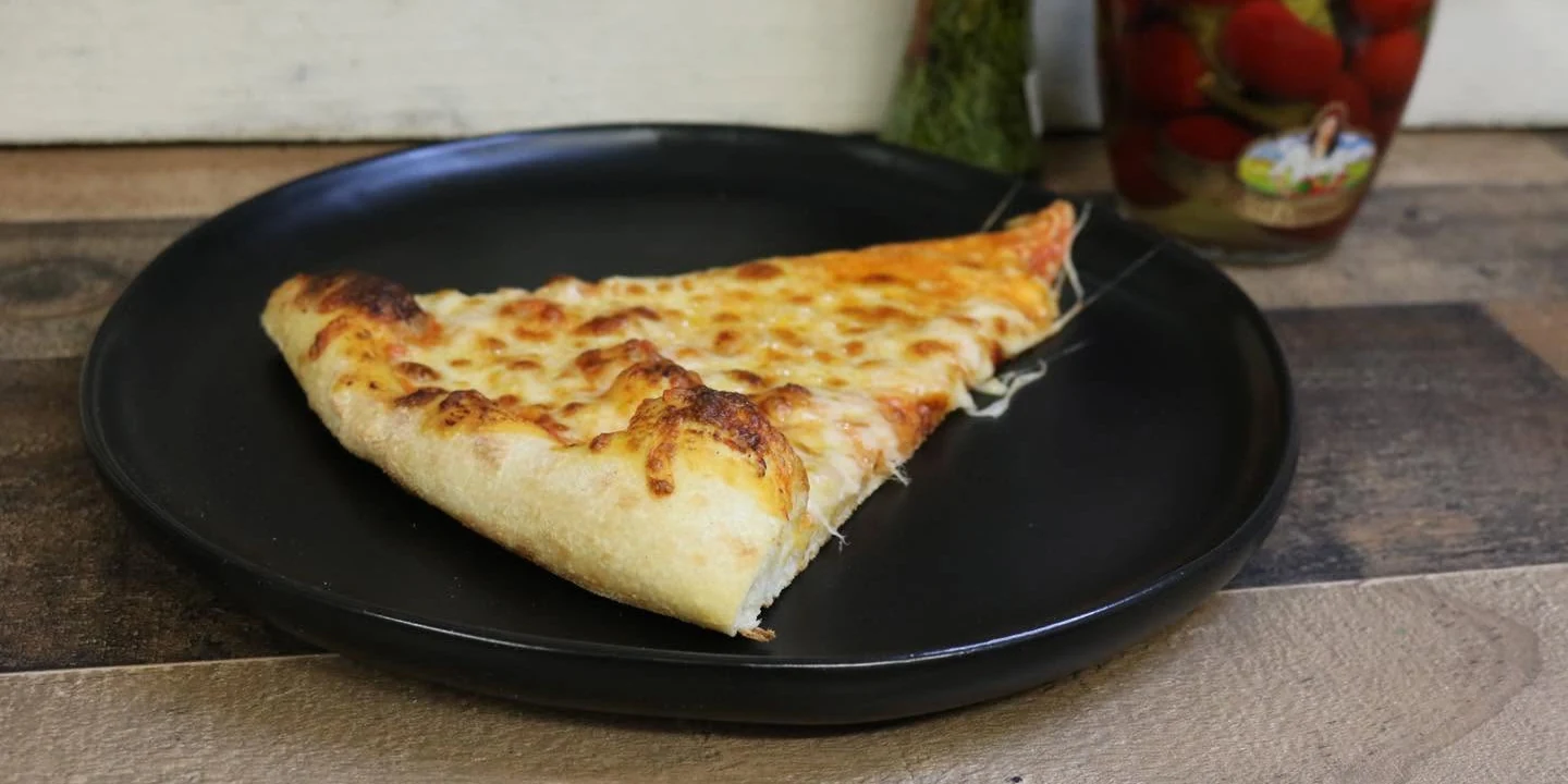 Slice of cheese pizza with stretching mozzarella on a black plate