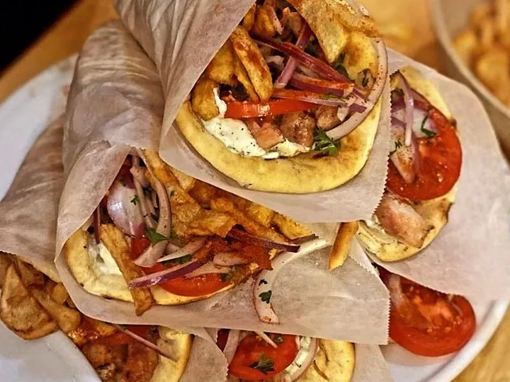 Chicken gyros wrapped in paper with tomato and red onion